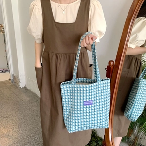Detail view of the blue and white checkered canvas tote bag with a purple woven label