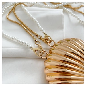 Close-up of golden shell-shaped clutch with pearl chain and metallic snake bone strap