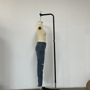 Detail view of high-waisted distressed blue denim jeans with ripped knee design on a mannequin