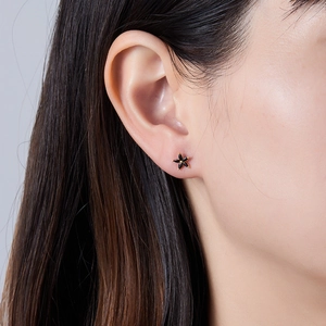 Detail of flower-shaped stud earrings featuring black petals and gold center on ear