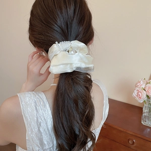 Detail of elegant satin scrunchie with pearls worn on a ponytail in soft indoor light