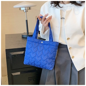 Close-up of blue heart-quilted tote bag held by a model in a minimalist interior setting