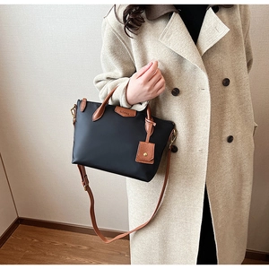 Detail of black nylon tote with brown leather handles worn with a beige trench coat
