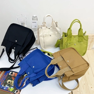 Five assorted canvas tote bags in black, beige, blue, green and brown on a white table