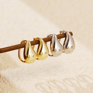 Artistic display of gold and silver teardrop earrings on a branch with soft shadows