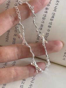 Close-up of S925 sterling silver bow bracelet featuring polished wavy links on book background