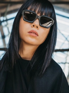 Close-up of black thick-frame sunglasses on model with modern angular design and dark lenses