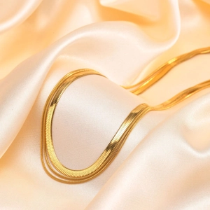 Detail of golden triple layered herringbone snake chains on elegant champagne silk fabric