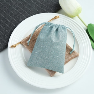 Blue and champagne glitter drawstring pouches for jewelry packaging on a white plate