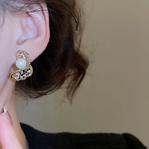 Close-up of golden hollow butterfly earrings with tiny zircon and a single pearl