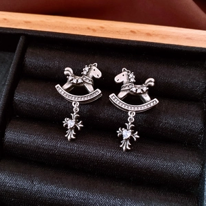 Macro view of vintage silver rocking horse and cross earrings with white zircon on black velvet
