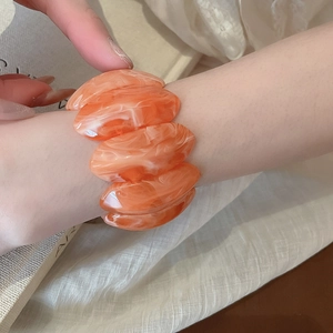 Detail of orange marble pattern acrylic stretch bracelet on a textured neutral surface