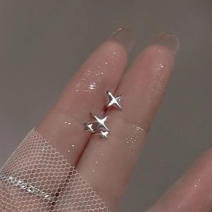Macro detail of silver four-pointed star stud earrings on a finger with lace background