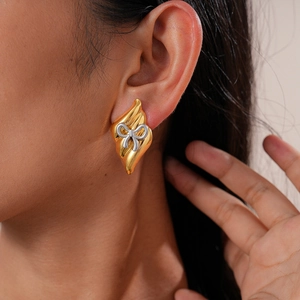 Détail de la boucle d'oreille dorée en forme de flamme avec nœud argenté portée par un mannequin