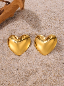 Gros plan de boucles d'oreilles cœur 3D plaquées or sur un fond de sable naturel