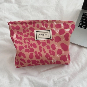 Dettaglio della borsa cosmetica rosa leopardata con logo su un lenzuolo bianco stropicciato