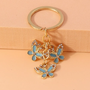 Golden butterfly keychain with blue enamel and sparkling crystals on orange background