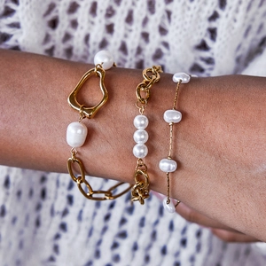 Close-up of stacked gold bow pearl bracelets on wrist with white knit background