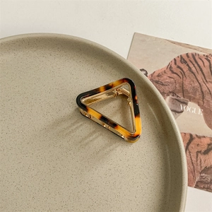 Close-up of a tortoiseshell acetate triangle hair claw with gold metal frame on a ceramic plate