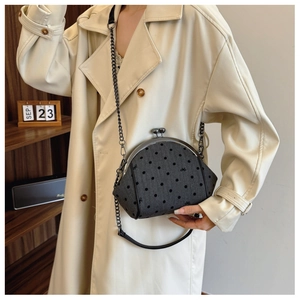 Deep grey polka dot shell bag with metal chain shown on model in a cozy indoor setting
