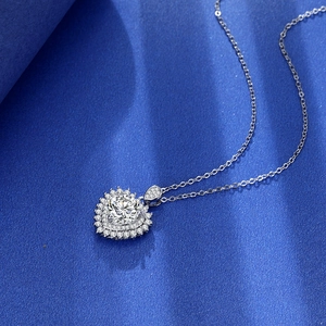 Macro shot of a 2-carat heart-shaped silver pendant with zircon insets on blue silk background