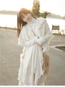 Detail of white knit poncho featuring decorative buttons and bohemian tassel fringe trim