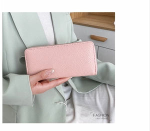 Close-up of pink pebbled leather long zipper wallet held by a woman in elegant suit