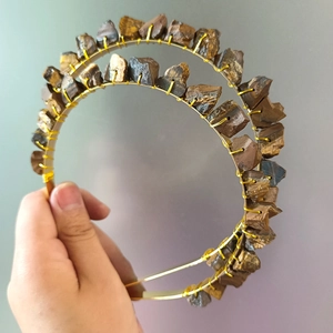 Handmade gold wire headband with raw tiger eye stones displayed on a grey background