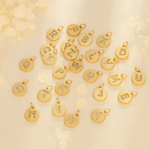 Golden copper pendants with inlaid zircon A-Z alphabets on elegant fabric background