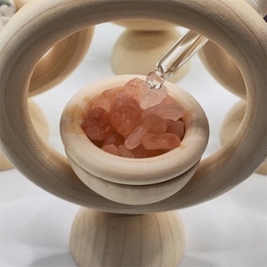 Detail of essential oil dropper pouring liquid onto pink salt crystals in wooden diffuser