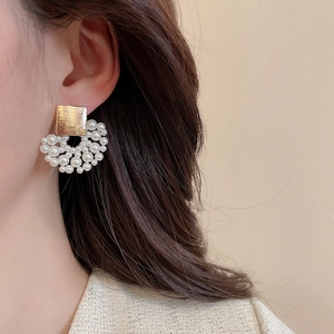 Close-up of pearl cluster earrings with golden brushed metal squares worn by a model