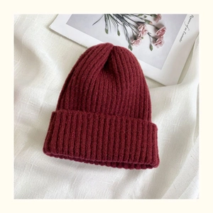 Detailed close-up of dark burgundy ribbed knit beanie texture on beige linen background