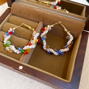 Detailed close-up of gold hoop earrings with colorful crystal beads and pearls in a wooden box