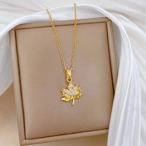 Detail of gold maple leaf pendant with glittering crystals on elegant beige jewelry box