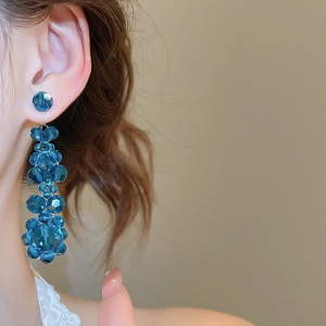 Close-up of elegant long blue crystal bead drop earrings worn by a model in soft light