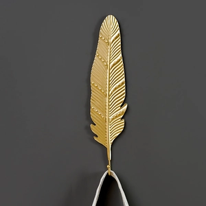 Nordic golden feather metal wall hook with intricate texture on dark grey background
