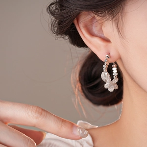 Close-up of silver butterfly hoop earrings with sparkling zircon inlay worn by a model