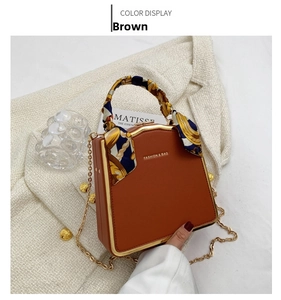 Detail of a brown structured box bag with golden metal frame and decorative silk scarf handle