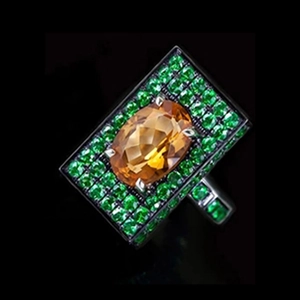 Macro detail of square black ring featuring an oval orange stone and green crystal pavé