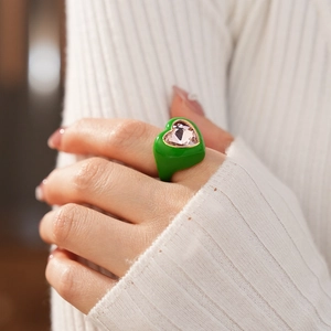 Detailed view of heart ring with green enamel and pink crystal on model hand