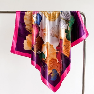 Detailed view of silky satin scarf with colorful ginkgo leaf print hanging on metal hanger