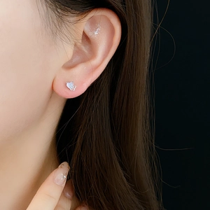 Close-up of silver heart and butterfly stud earrings with zircon stones worn by a model