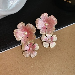 Detailed view of layered pink and gold flower earrings with brushed metal texture