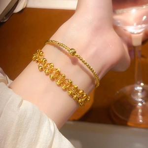 Detailed view of layered 24K gold-plated beaded bracelets on a wrist with elegant white sleeves