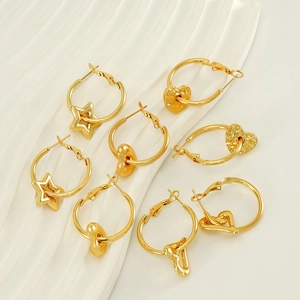 Polished 18K gold star and heart drop earrings on a white textured display stand