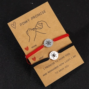 Detail of red and black woven friendship bracelets with silver spider web charms on card