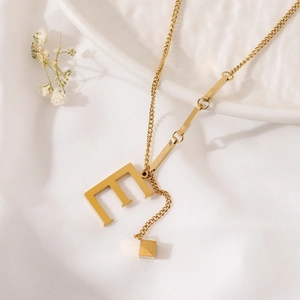 Macro detail of gold titanium necklace featuring letter E pendant and small cube charm