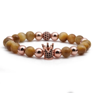 Detail of rose gold crown charm with micro-inlaid zircon on tiger eye stone bracelet