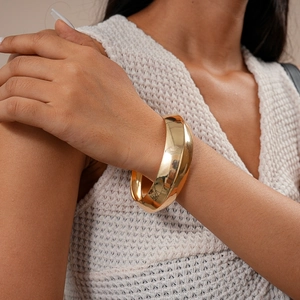 Dettaglio di un ampio bracciale a polsino in metallo dorato lucido su un polso