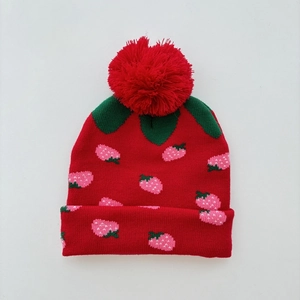 Detail of red strawberry knit hat featuring a fluffy pom-pom and green leaf patterns